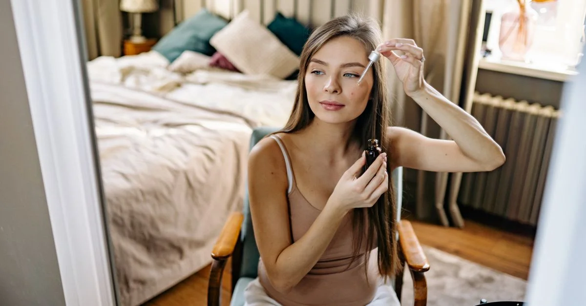 Une femme utilisant un compte-gouttes pour sa routine de soins de la peau dans une chambre confortable.