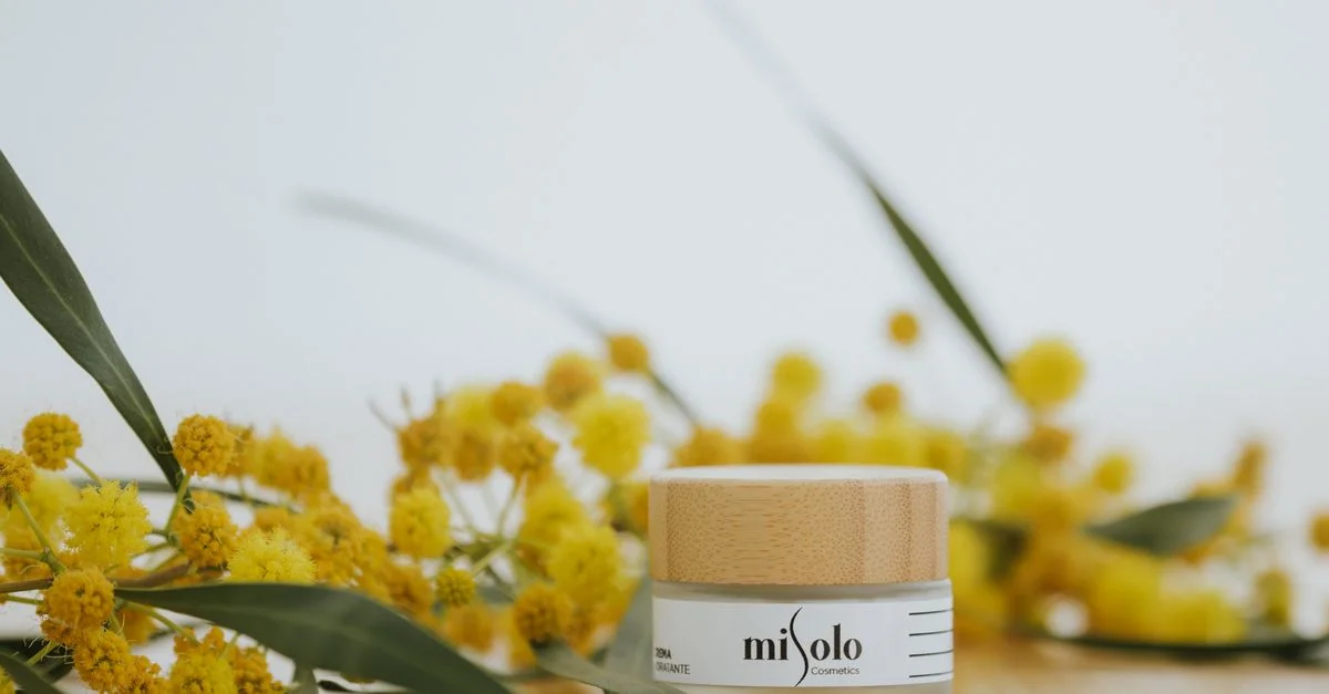 Gros plan d'un pot de crème visage naturelle entouré de fleurs jaunes dans un cadre de studio, idéal pour des thèmes de soins de la peau.