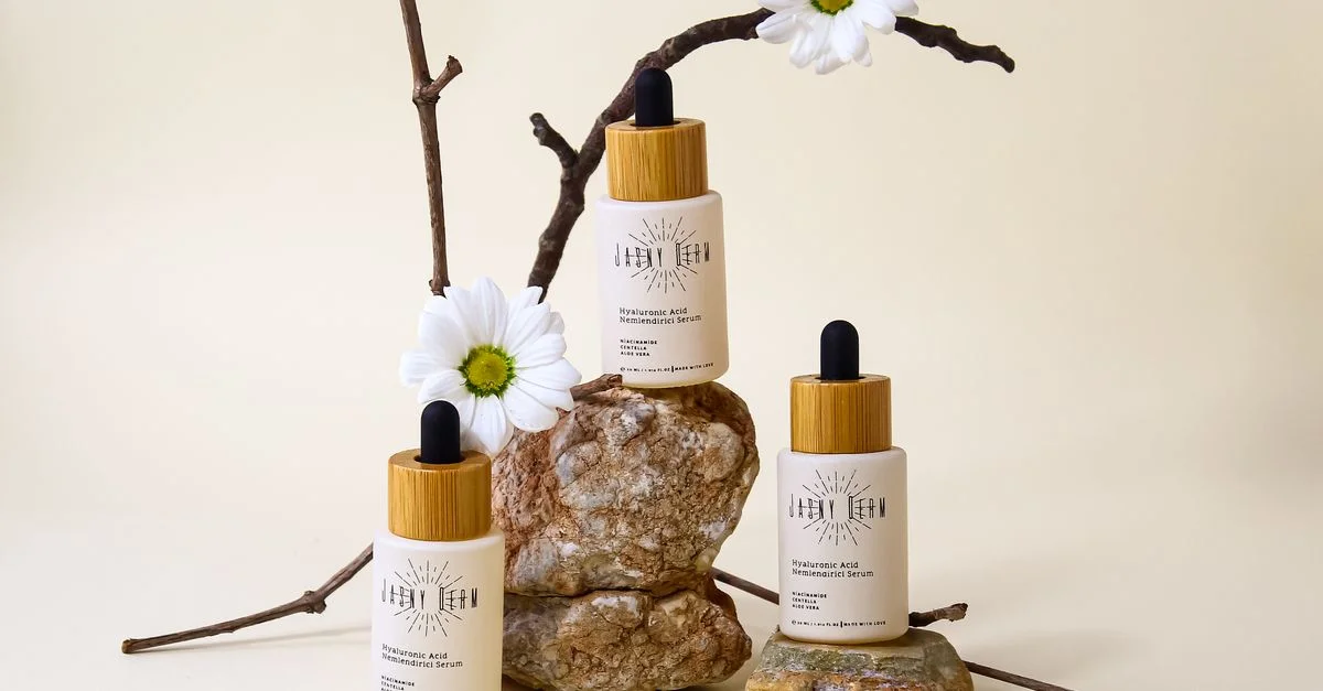 Flacons de sérum d'acide hyaluronique bio avec un arrangement floral et en pierre sur fond neutre.