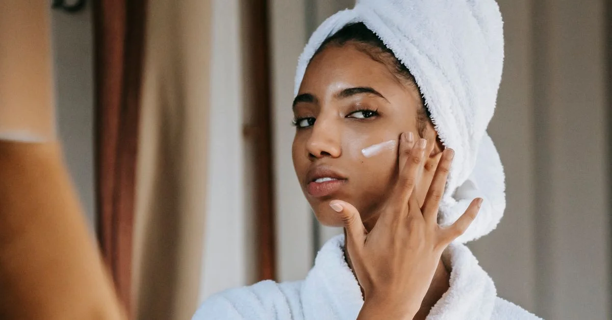 Jeune femme applique une crème dans une routine de soins apaisante, embrassant le soin de soi et le bien-être.