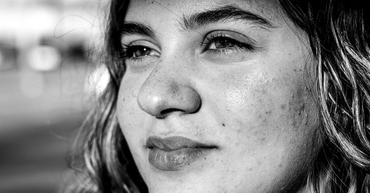 Portrait en gros plan, en noir et blanc, capturant l'expression pensive d'une femme baignée de soleil.